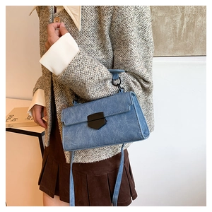 Detailed view of blue denim crossbody bag with black metal buckle worn with a beige jacket
