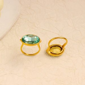 Detail of gold rings with oval green gemstone and faceted cut on beige background