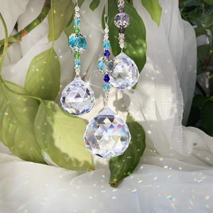 Close-up of 3 crystal prism balls with colorful beads hanging against green plants