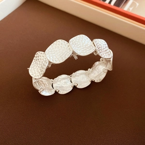 Close-up of hammered silver metallic links on a minimalist stretch bracelet over VOGUE magazine