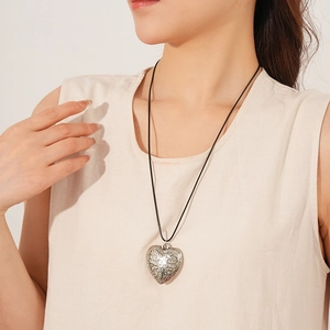 Detail of silver heart pendant with vintage relief pattern on black wax cord necklace