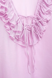 Detail of light pink blouse with ruffled neckline and bow tie design in soft fabric