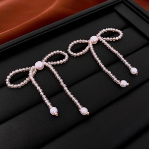 Detailed shot of bow-shaped beaded earrings with faux pearls on a black display tray