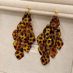 Macro detail of tortoiseshell resin petals and golden stud earrings on a textured tray
