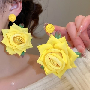 Detail of a large yellow fabric rose earring showing soft petal texture and green leaf accents