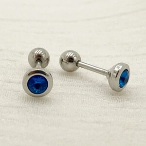Close-up of silver titanium steel barbell earrings with inlaid round blue zircon stones