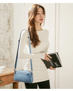 Detail of blue leather crossbody bag with dual zipper compartments and silver hardware