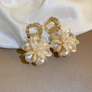 Détail de boucles d'oreilles fleurs en acrylique crème et cercles dorés sur soie