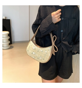 Detail of woven straw shoulder bag featuring floral embroidery and large bow detail