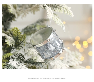 Silver drum Christmas ornament hanging on a snowy pine branch with festive bokeh lights