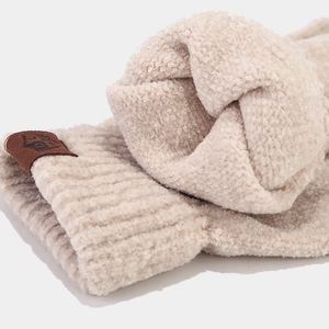 Gros plan sur maille côtelée beige épaisse avec un patch logo décoratif en cuir marron