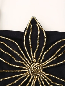 Detailaufnahme der goldenen Perlenstickerei auf schwarzem Stoff mit floralem Muster