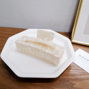 Détail d'une pince à cheveux rectangulaire en acétate marbré crème sur un plateau blanc