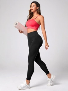 Side view of woman in red sports bra and black high waist seamless yoga leggings with mat