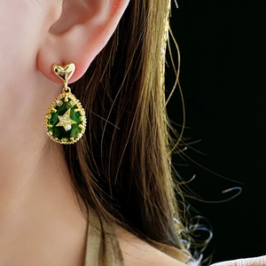 Detail of gold heart stud and green teardrop earring with star and pearl inlay