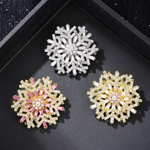 Detailed view of silver and gold snowflake brooches with cubic zirconia on black velvet