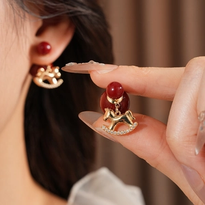 Close-up of gold-plated rocking horse earring with red bead and sparkling zircon inlay