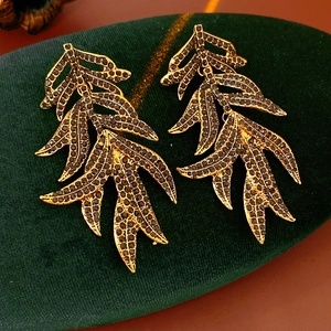 Close-up of golden leaf-shaped earrings with black diamonds on green velvet surface