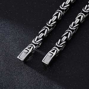 Macro detail of silver stainless steel braided chain link and clasp on a black background