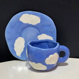 Close-up of handmade irregular blue ceramic coffee cup with white cloud patterns