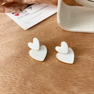 Detailed view of vintage gold-rimmed white heart stud earrings on a rustic wooden desk
