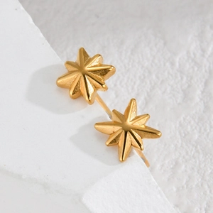 Macro shot of minimalist gold star stud earrings resting on a white textured stone surface