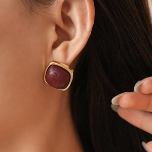 Close-up of geometric square leather stud earrings with burgundy texture and gold trim