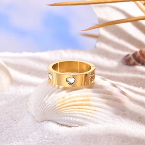 Close-up of gold stainless steel ring with heart zircons on a seashell at the beach