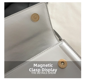 Detailed close-up of a golden circular magnetic snap closure on a white leather handbag