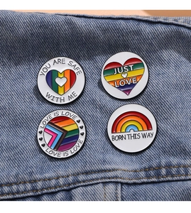 Close-up of four rainbow enamel pride badges on a denim jacket with text designs