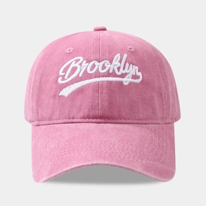 Close-up of white Brooklyn embroidery on washed pink cotton fabric of the baseball cap