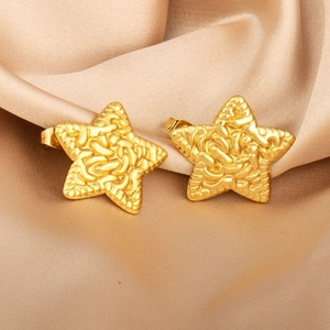 Macro shot of gold star stud earrings with relief texture on champagne silk fabric
