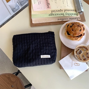 Detail of black quilted puffer cosmetic bag with woven label on a cafe table setting
