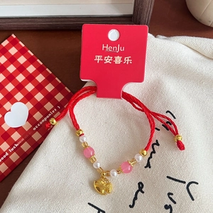 Close-up of red woven bracelet with pink glass beads and a golden pig zodiac pendant