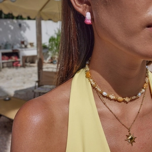 Close-up of a double-layered pearl necklace with sun pendant and pink gradient earrings