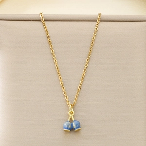 Detail of a gold stainless steel necklace with blue enamel fruit charms on a beige stand
