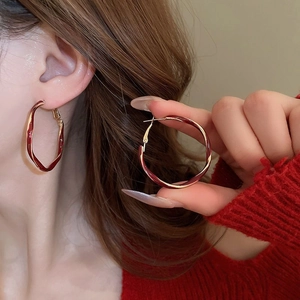 Close-up of model wearing twisted red hoop earrings with shiny metallic finish