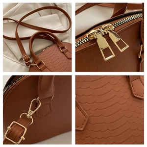Detail view of brown crocodile texture leather, gold hardware and zippers on a handbag