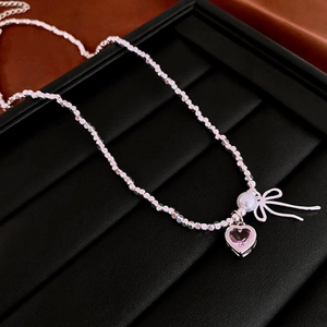 Detail of beaded bracelet with pink heart gemstone, white pearls and silver bow charm
