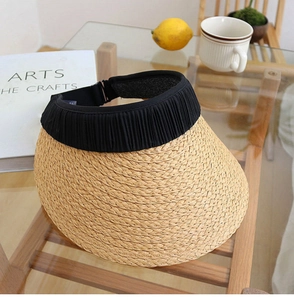 Close-up of woven straw sun hat with black pleated trim on a wooden table setup