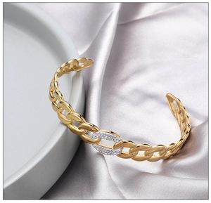 Detailed macro view of a gold-plated C-shape cuff bracelet with zircon insets on ceramic
