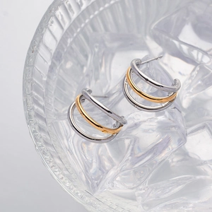 Detail view of two-tone gold and silver C-shaped hoop earrings resting on clear ice cubes