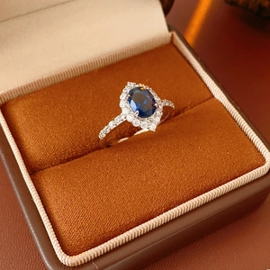 Detail of blue sapphire oval ring with white diamond halo on orange velvet cushion