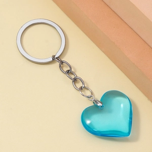 Close-up of translucent cyan resin heart keychain on a textured beige surface