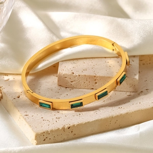 Détail d'un bracelet en acier doré 18K avec zircons verts sur pierre beige élégante