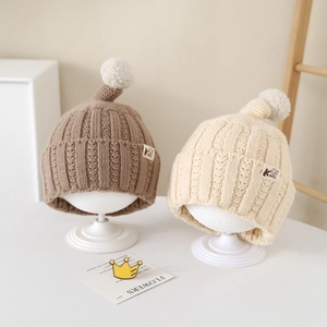Close-up of khaki and cream knitted toddler hats with pointed top and faux fur ball