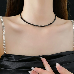 Close-up of minimalist black beaded necklace worn by a model on a dark background