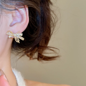 Close-up of elegant bow-shaped gold earrings with sparkling zircon stones on model