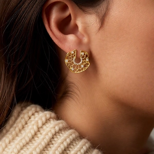 Close-up of a gold hollow round earring with zircons worn with a beige sweater