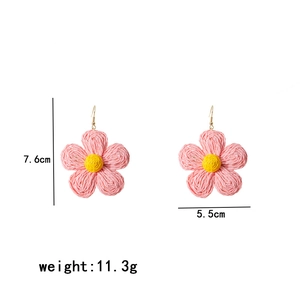 Detail view of woven raffia flower earrings in pink and yellow with size and weight info